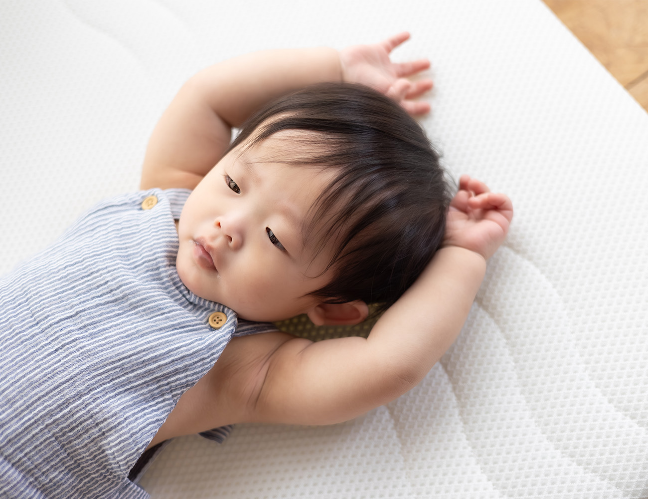 Resting baby with his arms up relaxing on breathable crib mattress